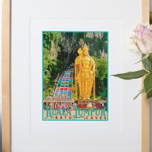 May include: A framed print featuring a vibrant image of the Batu Caves in Kuala Lumpur, Malaysia. The artwork showcases a golden statue and colorful steps leading to the caves, with the text "KUALA LUMPUR BATU CAVES" at the bottom. The frame is light wood.