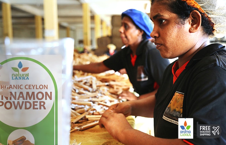 May include: Two people working in a factory, sorting and packaging cinnamon sticks. A bag of "Natural Lanka Organic Ceylon Cinnamon Powder" is in the foreground.