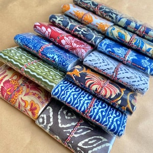 May include: A selection of fabric bundles, each wrapped and tied with twine. The fabrics display various patterns, including floral and geometric designs, in a range of colours such as red, blue, green, and orange. The bundles are neatly arranged.