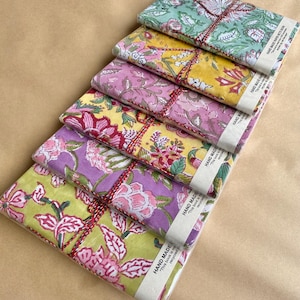 May include: A stack of notebooks featuring floral designs in green, yellow, pink, and purple. Each notebook is wrapped and tied with twine. The packaging includes the text "HAND MADE" and "This book is made recycled".
