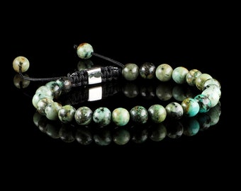 Op de afbeelding: Een turquoise edelsteen armband met een zwart koord en een zilveren sluiting. De armband is gemaakt van ronde kralen en heeft een eenvoudig ontwerp.