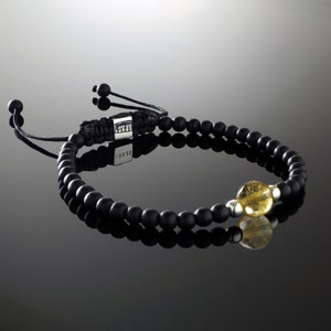 Op de afbeelding: Zwarte kralen armband met een zilveren schuifgesp en een gele edelsteen kraal. De armband heeft een zwart koord met het woord "LOVE" in zilveren letters.