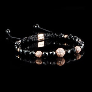 Op de afbeelding: Zwarte kralen armband met roségouden accenten en een klein bedeltje met het woord "MAXSE" erop.