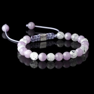 May include: A purple and clear crystal beaded bracelet with a silver clasp and a purple cord. The bracelet is tied with a knot and has the word "FAKSÉ" on the clasp.