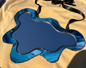 May include: A blue stained glass mirror in the shape of a cloud with a black ribbon hanging from the top.