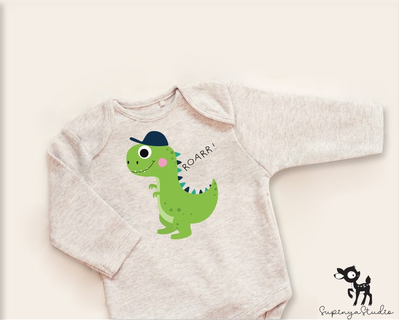 K&ouml;nnte beinhalten: Ein grauer lang&auml;rmeliger Baby-Strampler mit einem gr&uuml;nen Dinosaurier, der eine blaue Baseballkappe tr&auml;gt. Der Dinosaurier l&auml;chelt und sagt "ROARR!"