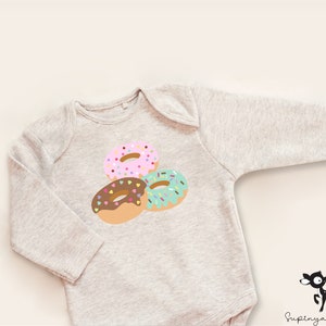 May include: A gray long-sleeved baby onesie with a graphic of three donuts with colorful sprinkles. The donuts are pink, brown, and green.