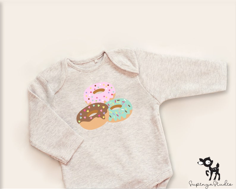 May include: A gray long-sleeved baby onesie with a graphic of three donuts with colorful sprinkles. The donuts are pink, brown, and green.