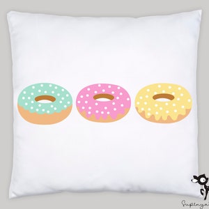 May include: Three colorful donuts with white sprinkles on a white pillow. The donuts are green, pink, and yellow.