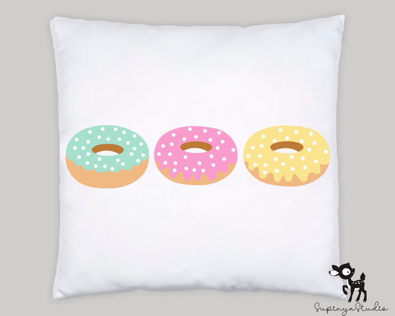 May include: Three colorful donuts with white sprinkles on a white pillow. The donuts are green, pink, and yellow.