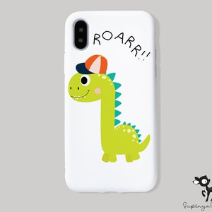 K&ouml;nnte beinhalten: Weisse Handyh&uuml;lle mit einem gr&uuml;nen Dinosaurier, der eine rot-orange Baseballkappe tr&auml;gt. Der Dinosaurier l&auml;chelt und sagt "ROARR!!" in schwarzer Schrift.