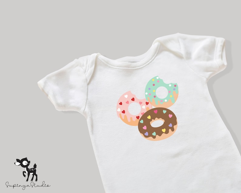 May include: White baby onesie featuring a design of three donuts. The donuts are pink with hearts, green with sprinkles, and brown with chocolate icing and sprinkles.