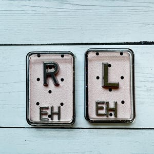 May include: Two rectangular, clear-framed accessories with a pink background. The left one has the letter "R" above the letters "EH". The right one has the letter "L" above the letters "EH".