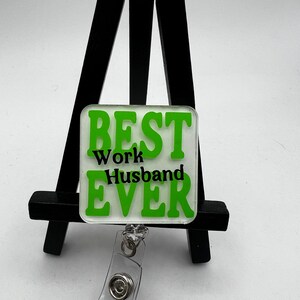 Puede incluir: Portagafete verde y blanco con el texto "BEST Work Husband EVER" en letras negras.