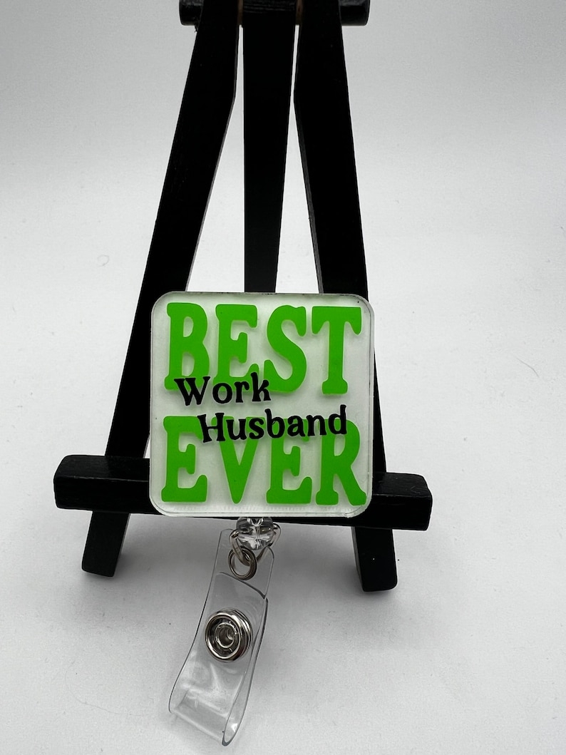 Puede incluir: Portagafete verde y blanco con el texto "BEST Work Husband EVER" en letras negras.
