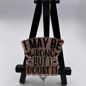 May include: A pink glitter badge holder with the text "I may be wrong but I doubt it" in black lettering. The badge holder is attached to a silver retractable badge reel.