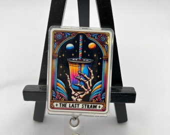 Op de afbeelding: Een kleurrijke badgehouder met een cartoonafbeelding van een skelethand die een beker met een rietje vasthoudt. De afbeelding is omgeven door een decoratief kader en de tekst "The Last Straw" is onder de afbeelding gedrukt.