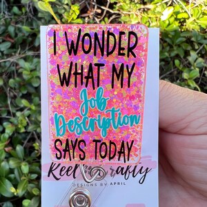 May include: Pink glitter badge holder with the text "I wonder what my job description says today" and the text "Keel crafty designs by April" below. The badge holder has a clear plastic clip and is decorated with glitter.