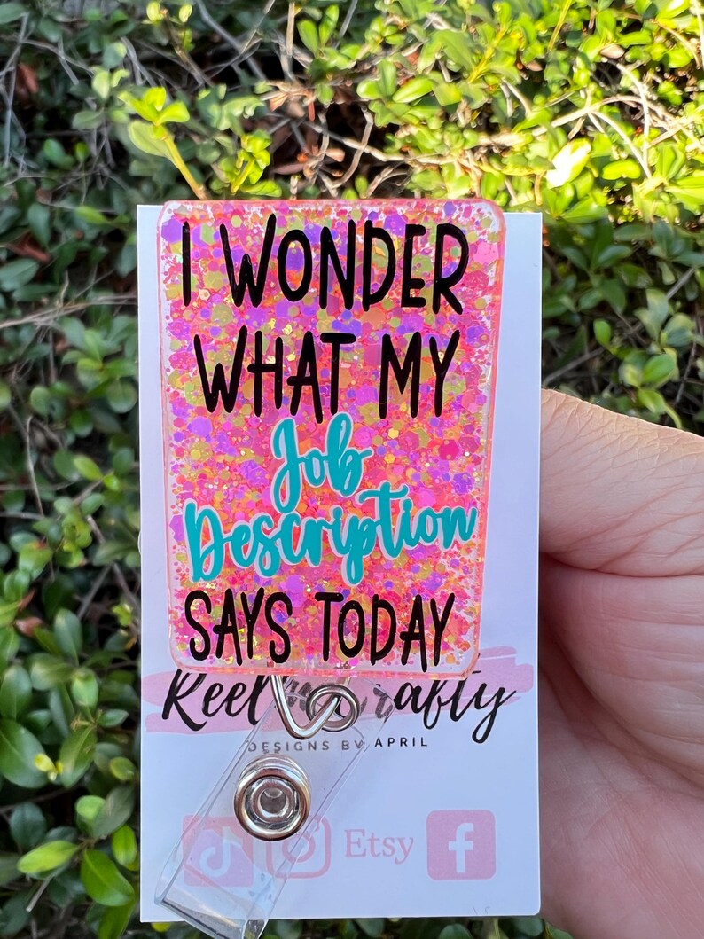 May include: Pink glitter badge holder with the text "I wonder what my job description says today" and the text "Keel crafty designs by April" below. The badge holder has a clear plastic clip and is decorated with glitter.