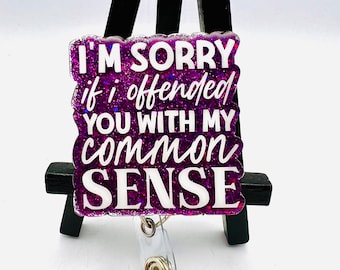 Pode incluir: Um porta-crachá roxo brilhante com o texto "I'M SORRY if I offended YOU WITH MY common SENSE" em letras brancas. O porta-crachá tem uma alça de plástico transparente e um clipe de metal.
