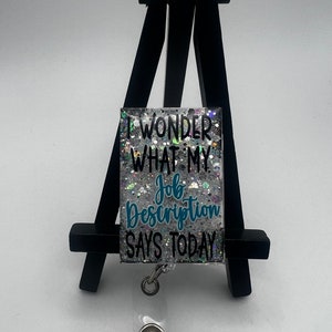 May include: A silver glitter badge holder with a teal blue inscription that reads "I wonder what my job description says today".