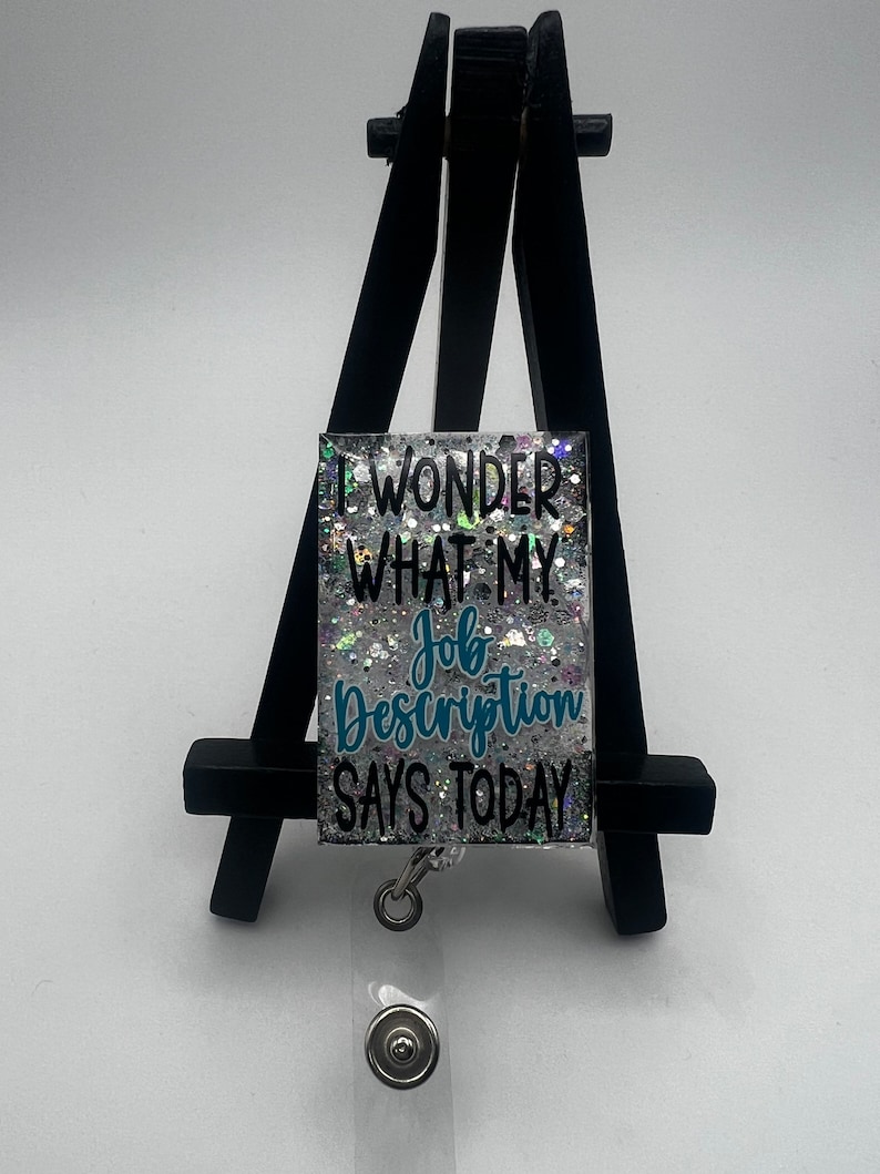 May include: A silver glitter badge holder with a teal blue inscription that reads "I wonder what my job description says today".