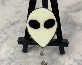 May include: A white alien face with black eyes on a silver retractable badge reel.