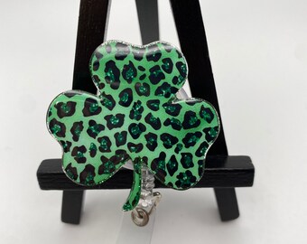 May include: A green and black leopard print shamrock shaped badge reel. The shamrock is made of clear plastic with a glitter finish.