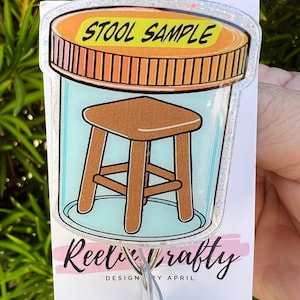 May include: A novelty badge reel featuring a cartoon illustration of a stool inside a jar with the words "STOOL SAMPLE" on the lid. The badge reel has a clear plastic retractable cord and a decorative border.