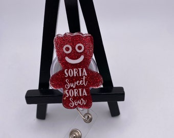 May include: Red glitter gummy bear charm with a white smiling face and the text "Sorta Sweet Sorta Sour" attached to a clear retractable badge holder.