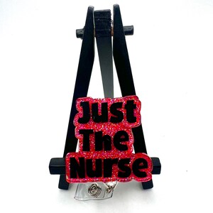 May include: A pink glitter badge reel with black text that reads "Just The Nurse".