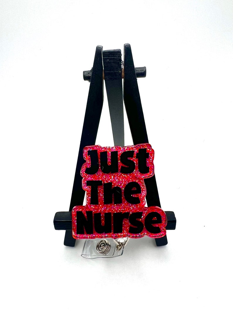 May include: A pink glitter badge reel with black text that reads "Just The Nurse".