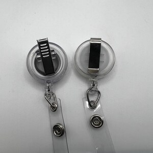 May include: Two clear retractable badge holders with silver clips and a silver ring at the bottom of each holder.