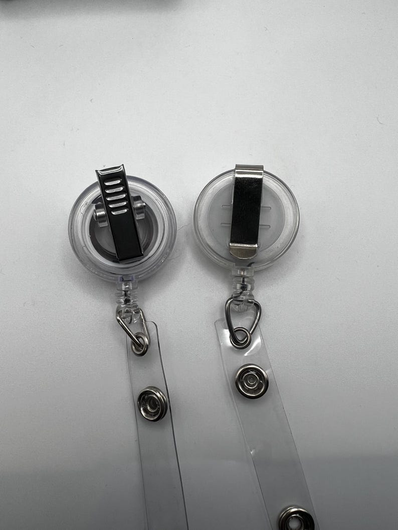 May include: Two clear retractable badge holders with silver clips and a silver ring at the bottom of each holder.