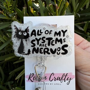 May include: A white glitter badge holder with a black cat illustration and the text "All of my systems are nervous".