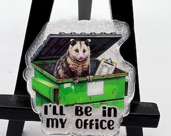 May include: A white and green glitter badge holder with a picture of a possum in a green dumpster. The text "I'll be in my office" is printed on the badge holder.