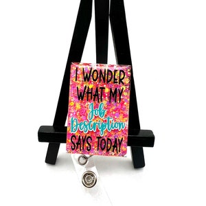 May include: A pink and yellow glitter badge holder with the text "I wonder what my job description says today".