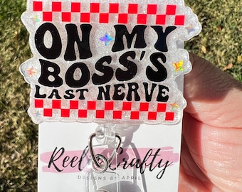 May include: A white glitter badge holder with a red and white checkered border. The text "On My Boss's Last Nerve" is in black with glitter accents. The badge holder is attached to a clear retractable badge reel.