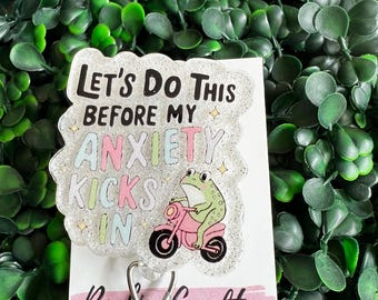 May include: A silver glitter badge holder with a green frog riding a pink motorcycle. The badge holder has the text "Let's do this before my anxiety kicks in".