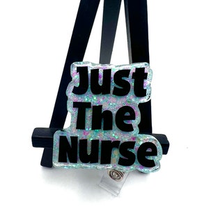 May include: A light blue and iridescent glitter badge holder with a black text overlay that reads "Just The Nurse".