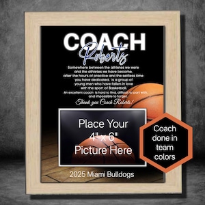 May include: A framed print with a basketball theme. The print features a black background with white text that reads "Coach Roberts". The text is surrounded by a basketball and a space to place a 4x6 inch photo. The bottom of the print reads "2025 Miami Bulldogs".