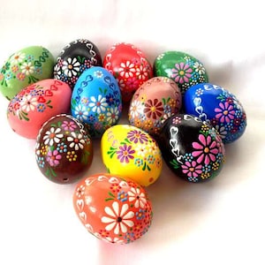 Può includere: Una collezione di 12 uova di Pasqua dipinte a mano con motivi floreali in vari colori, tra cui rosa, blu, verde, giallo, rosso e nero.