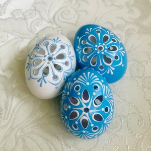 Könnte beinhalten: Drei aufwendig verzierte Ostereier. Zwei sind blau mit weißen Blumenmustern bemalt, eines ist weiß mit blauen Blumenmustern.