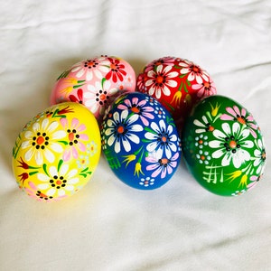 Könnte beinhalten: Fünf handbemalte Ostereier mit Blumendesigns. Die Eier sind in den Farben Gelb, Rosa, Rot, Blau und Grün bemalt.