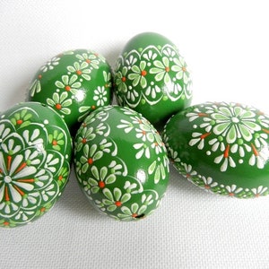Op de afbeelding: Vijf groene paaseieren versierd met witte en oranje bloemmotieven.