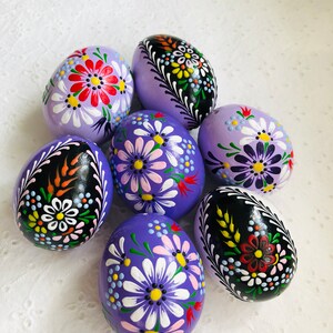 Può includere: Sei uova di Pasqua dipinte a mano con motivi floreali. Le uova sono dipinte in tonalità di viola, nero e bianco con intricati motivi floreali.