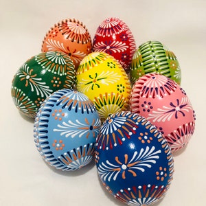 Può includere: Otto uova di Pasqua dipinte a mano in vari colori, tra cui verde, blu, giallo, rosa e rosso. Ogni uovo presenta intricati disegni floreali bianchi.
