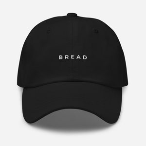 May include: A black dad hat with a white embroidered word "BREAD" on the front.