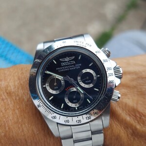 May include: A stainless steel Invicta Chrono-Master watch with a black dial. The watch has three sub-dials, a date display, and a tachymeter bezel. The watch is on a stainless steel bracelet.