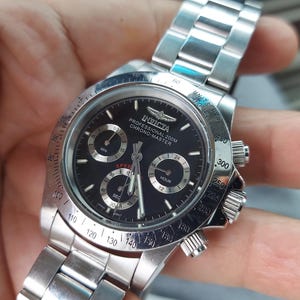 May include: A silver Invicta Professional 200M Chrono Master watch with a black dial. The watch features three sub-dials, a date display, and a stainless steel strap. The watch has a round face and a rotating bezel with numbers.